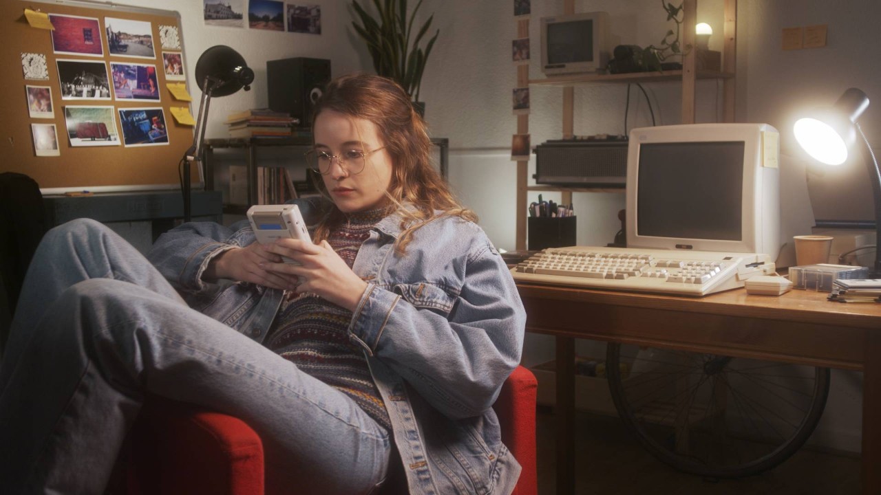 Young woman wearing jeans and a jean jacket playing a handheld game in an 80s-themed bedroom at Porros’s Custom Interiors near Worcester, MA